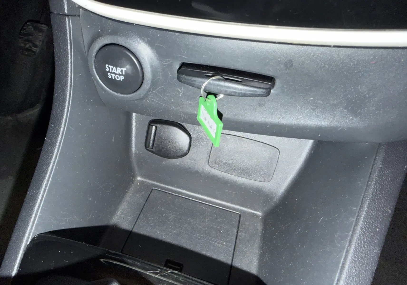 Gros plan sur la console centrale noire d'une Renault Clio Estate IV 2015, montrant bouton start/stop et clé avec porte-clé vert.