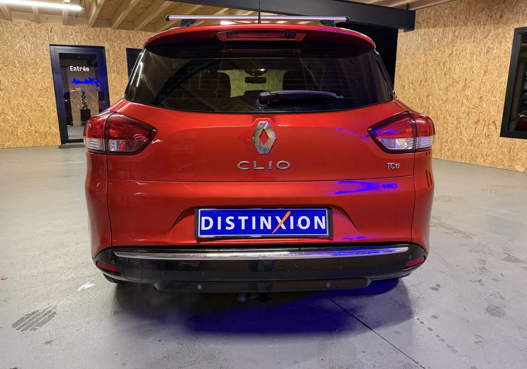 Vue arrière d'une Renault Clio Estate IV rouge avec attelage et logo TCe visible dans un garage.