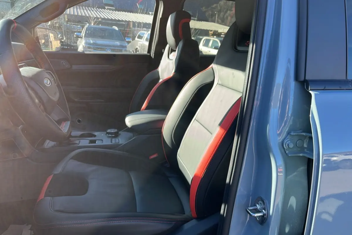 Vue intérieure côté conducteur du Ford Ranger Raptor 2025 gris commandeur, sièges sport cuir noir avec surpiqûres rouges.