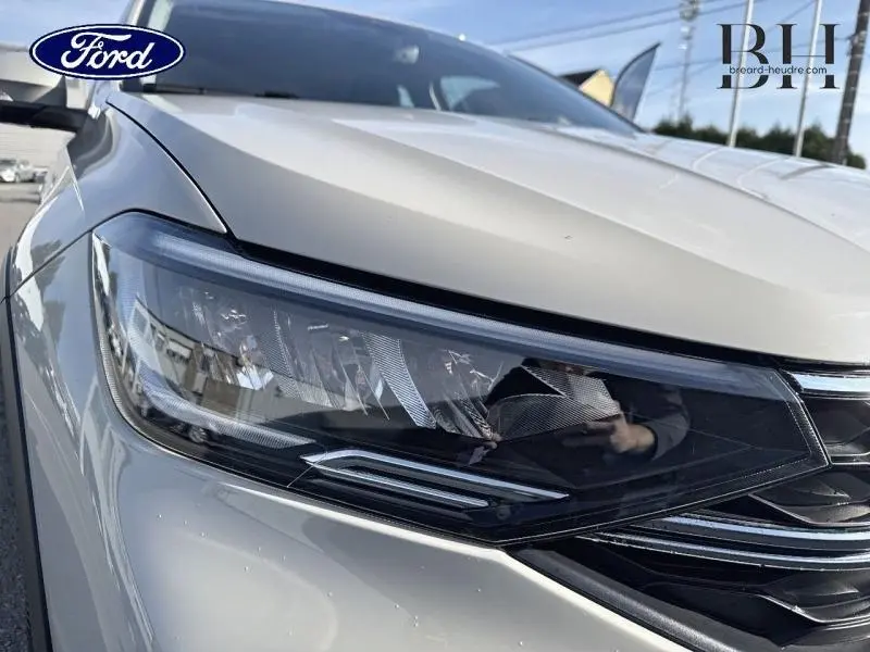 Gros plan sur le phare avant droit d’un Volkswagen Taigo blanc pur, soulignant les détails modernes du bloc optique.