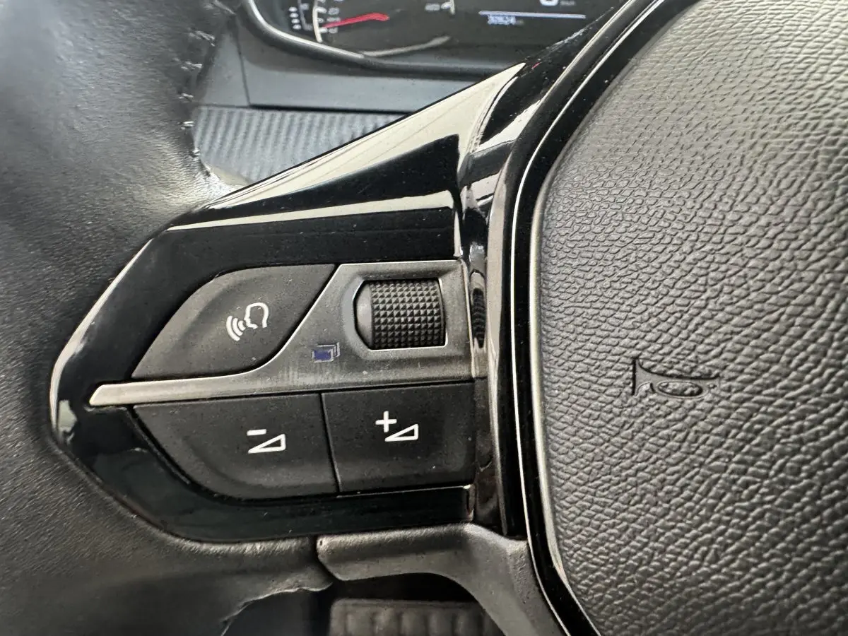 Gros plan sur les commandes vocales et volume du volant cuir noir de la Peugeot 208 PureTech 100 S&S Active Business.