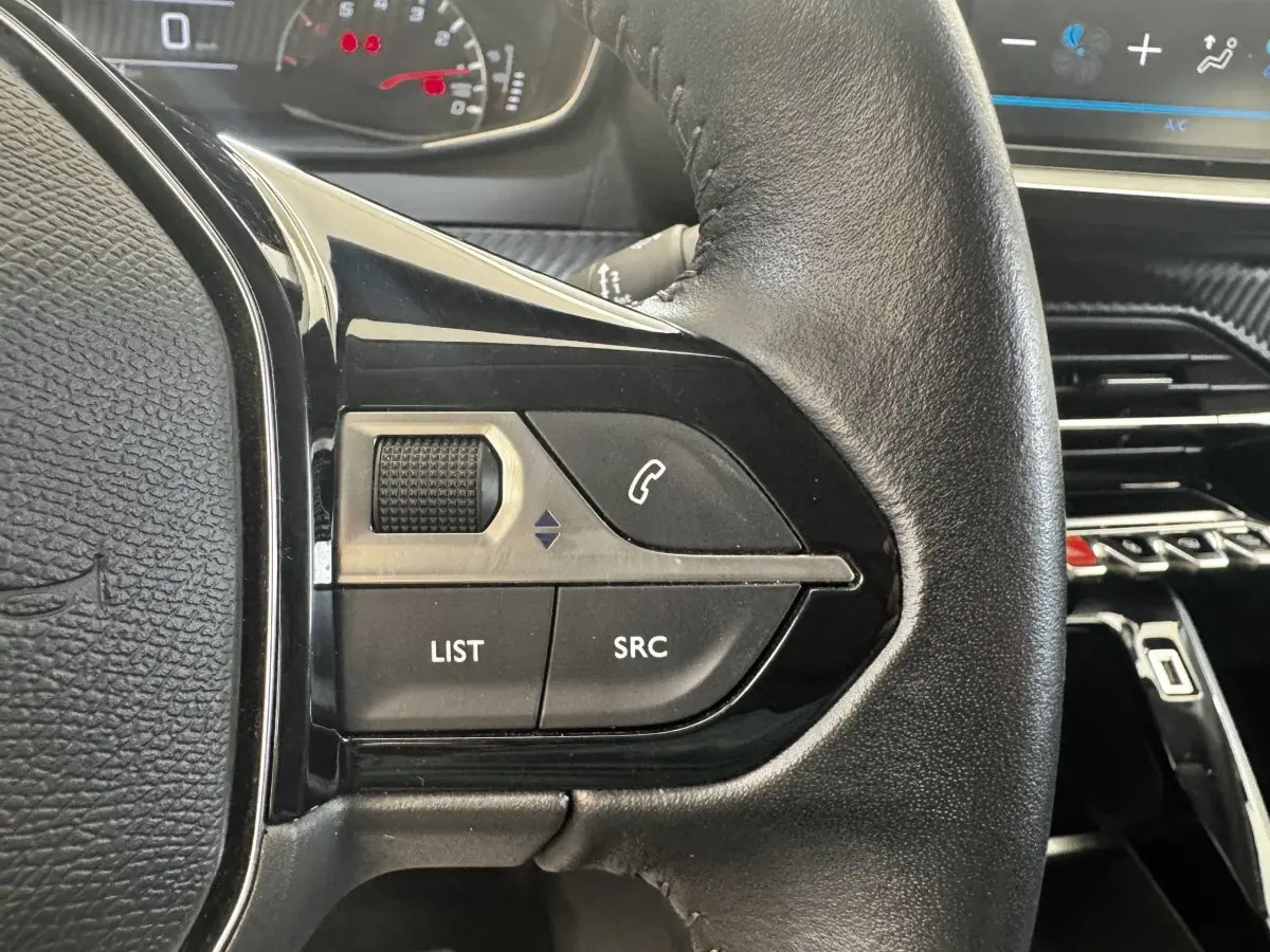 Gros plan sur le volant cuir noir de la Peugeot 208 blanc, avec commandes audio et téléphone intégrées.