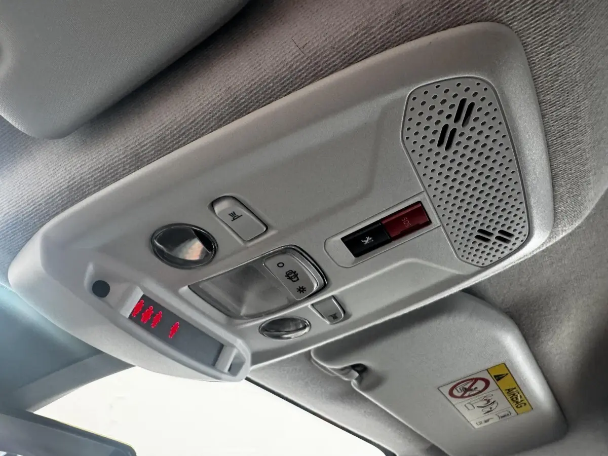 Vue intérieure du plafonnier gris clair de la Peugeot 208 blanc, avec commandes d’éclairage et bouton SOS rouge.