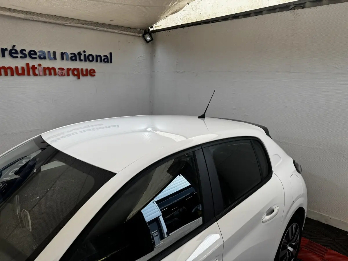 Vue 3/4 arrière droite d'une Peugeot 208 blanche 2020 garée en intérieur avec vitres teintées et antenne de toit.