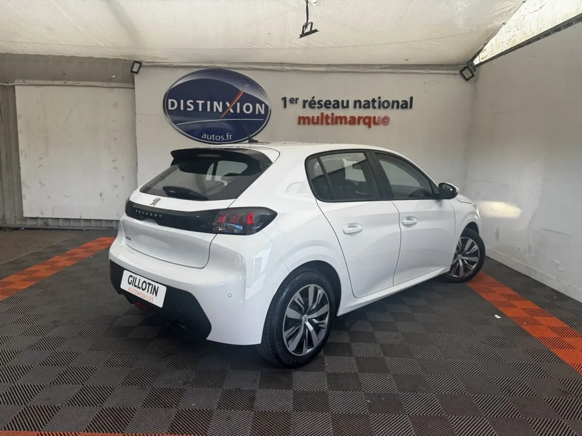 Peugeot 208 blanc vue 3/4 arrière droit en intérieur, avec jantes alliage et bande noire distinctive sur la porte.