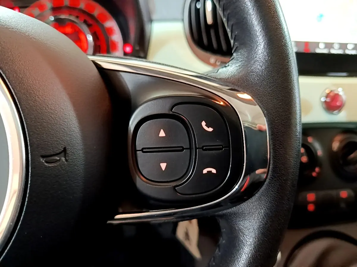 Gros plan sur les commandes du volant cuir noir de la Fiat 500 Lounge 2019, avec tableau de bord en arrière-plan.