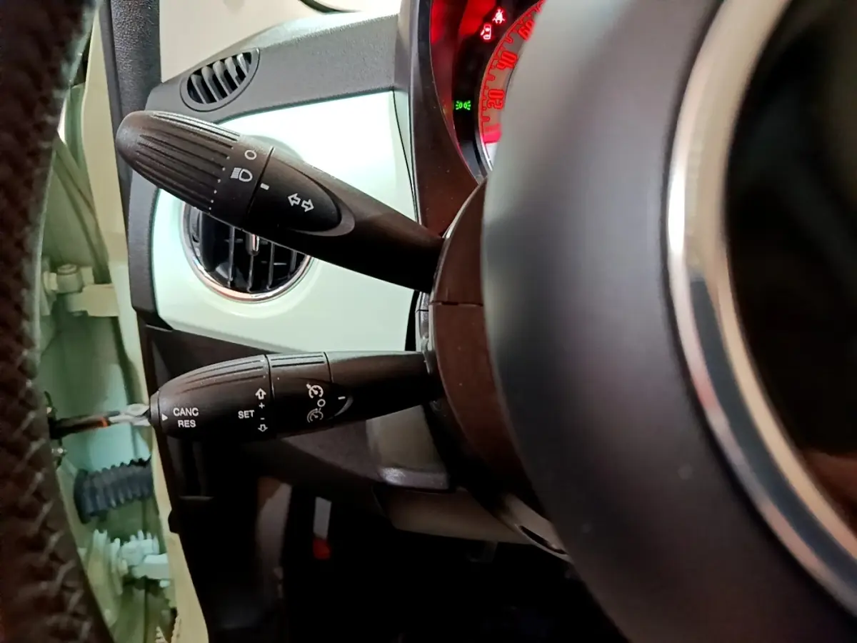 Détail des commandes au volant côté gauche d'une Fiat 500 Lounge 2019 vert clair, avec tableau de bord partiellement visible.