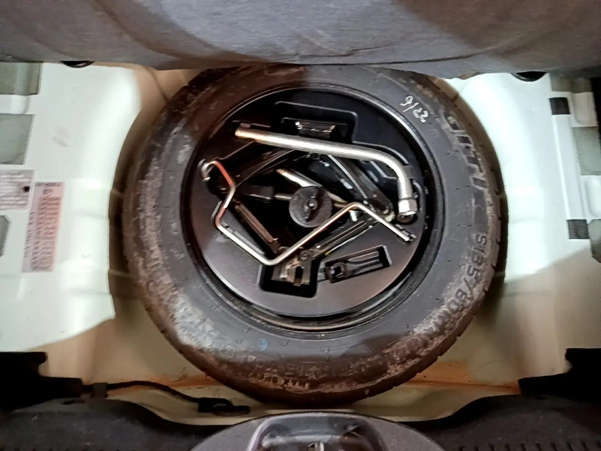 Roue de secours noire avec outils de changement dans le coffre d'une FIAT 500 verte, vue de dessus.