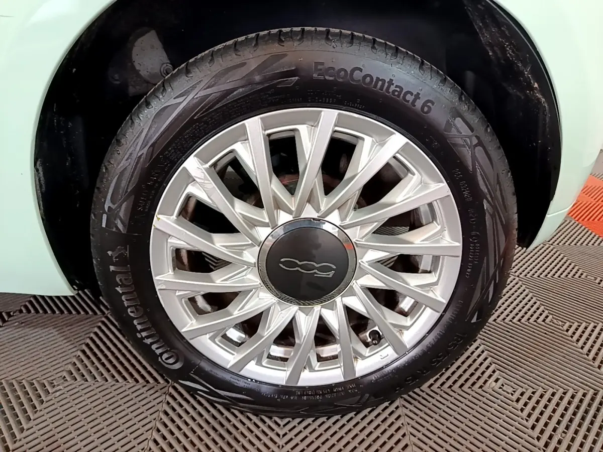 Gros plan sur la roue avant gauche d'une FIAT 500 verte, mettant en valeur la jante argentée au design étoilé.