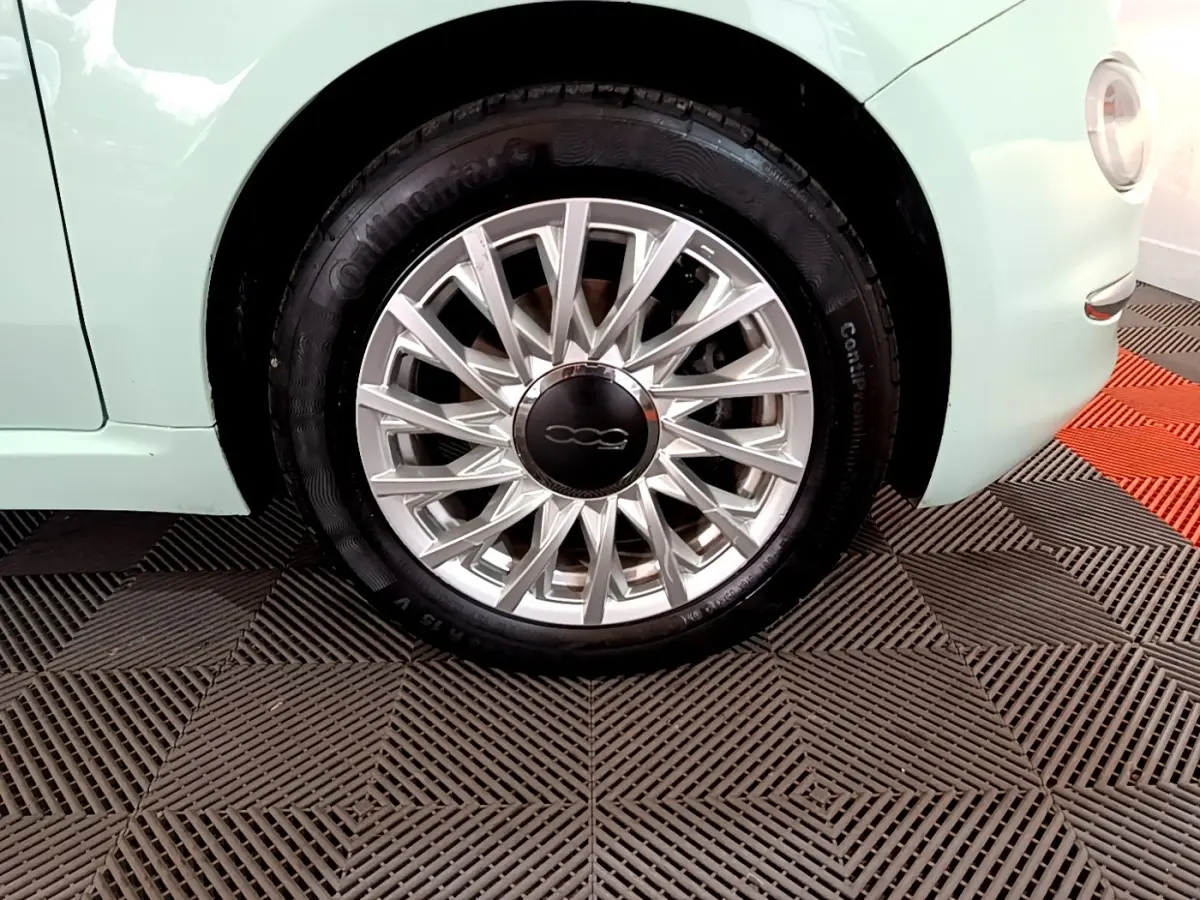 Gros plan sur la roue avant droite d'une FIAT 500 verte pastel, mettant en valeur la jante argentée au design fin.