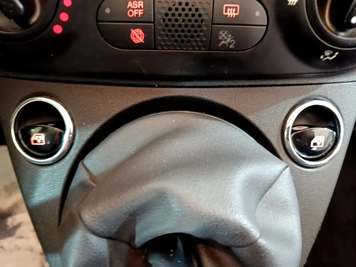 Gros plan sur la console centrale de la Fiat 500 Lounge 2019, montrant les commandes des vitres électriques et le soufflet de levier de vitesse noir.