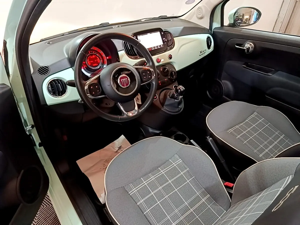 Vue intérieure côté conducteur de la FIAT 500 verte, tableau de bord clair et sièges gris à motifs carreaux.