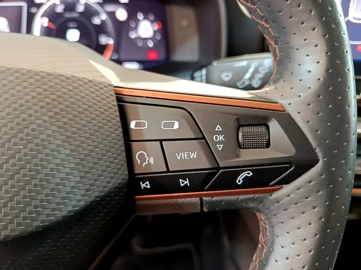 Gros plan sur les commandes noires et orange du volant en cuir perforé du CUPRA Formentor 2023, affichage digital en arrière-plan.