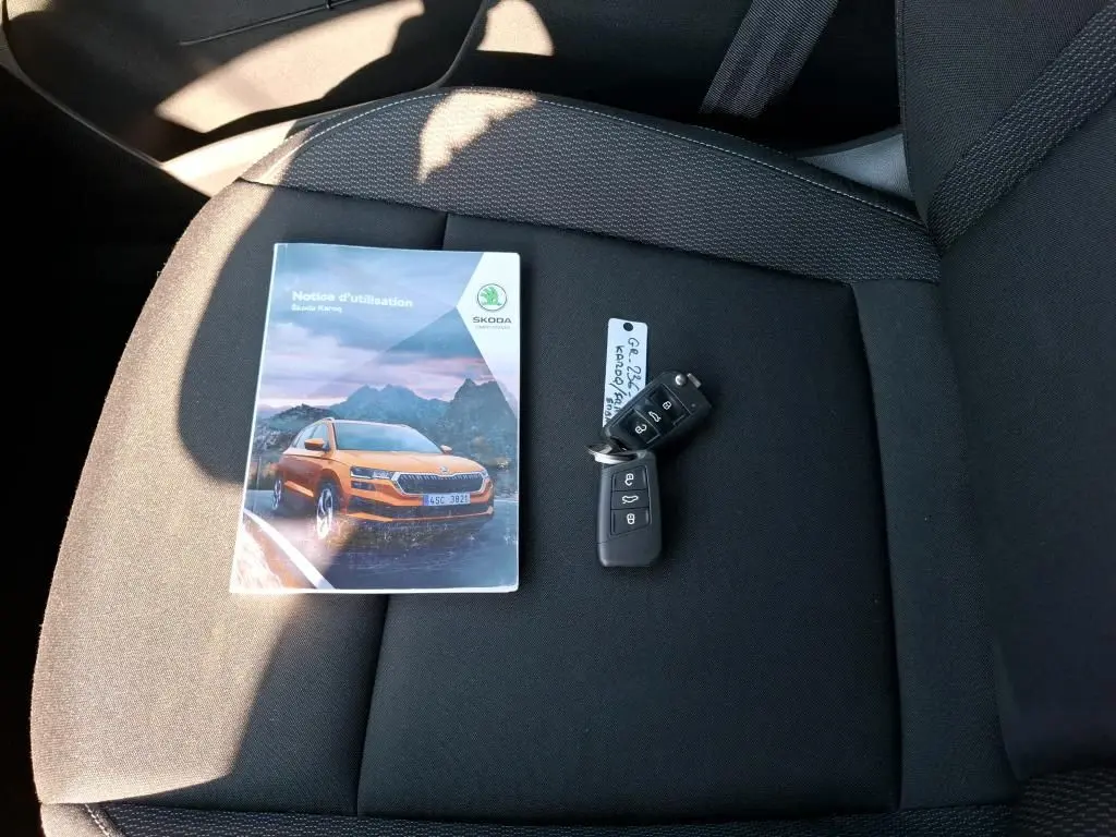Vue rapprochée sur siège noir avec notice Skoda Karoq orange et clé de voiture noire posées dessus.