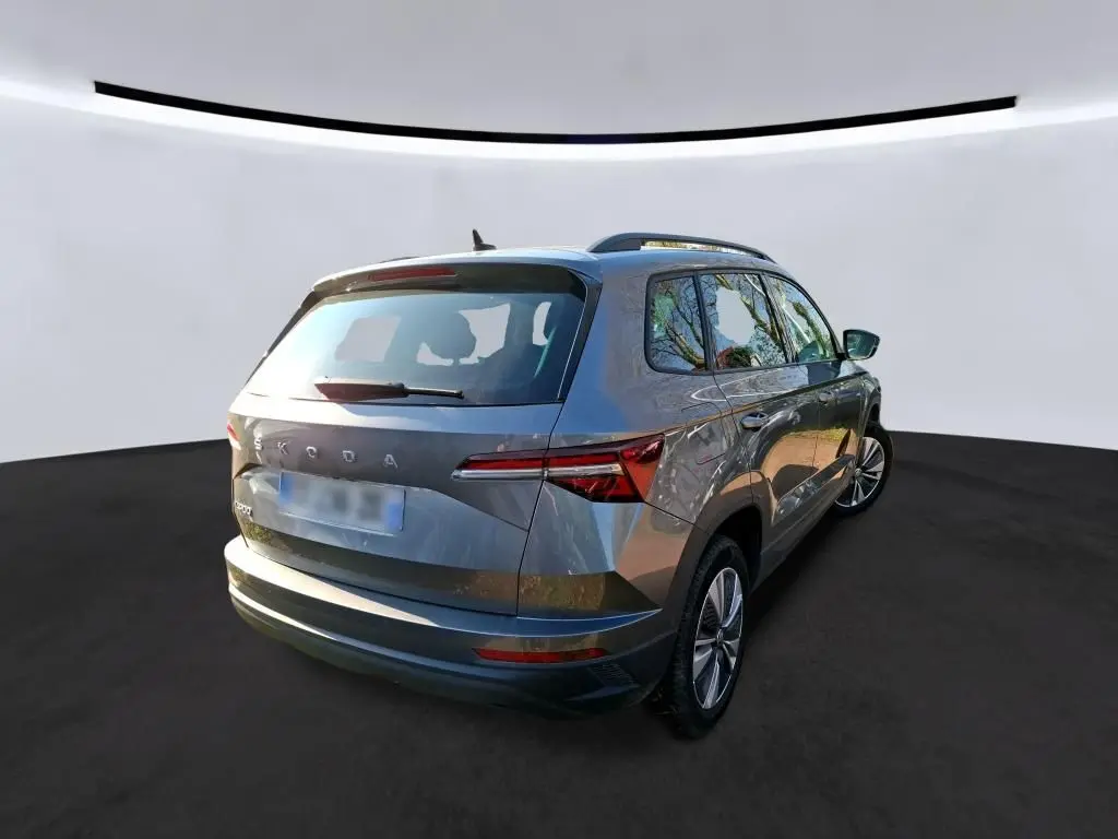 Vue 3/4 arrière droite d'un Skoda Karoq gris 2023 avec jantes alu 17 pouces et toit avec barres de pavillon noires.