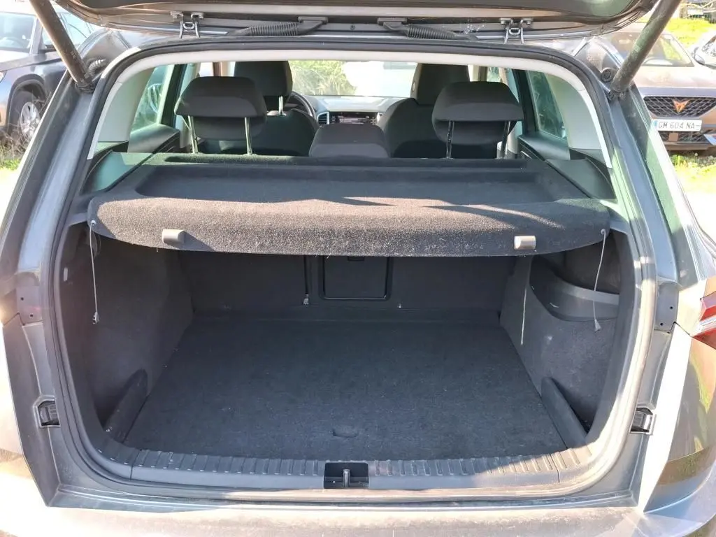 Vue arrière du coffre ouvert d'un SKODA KAROQ gris 2023, montrant l'espace de chargement avec cache-bagages déployé.