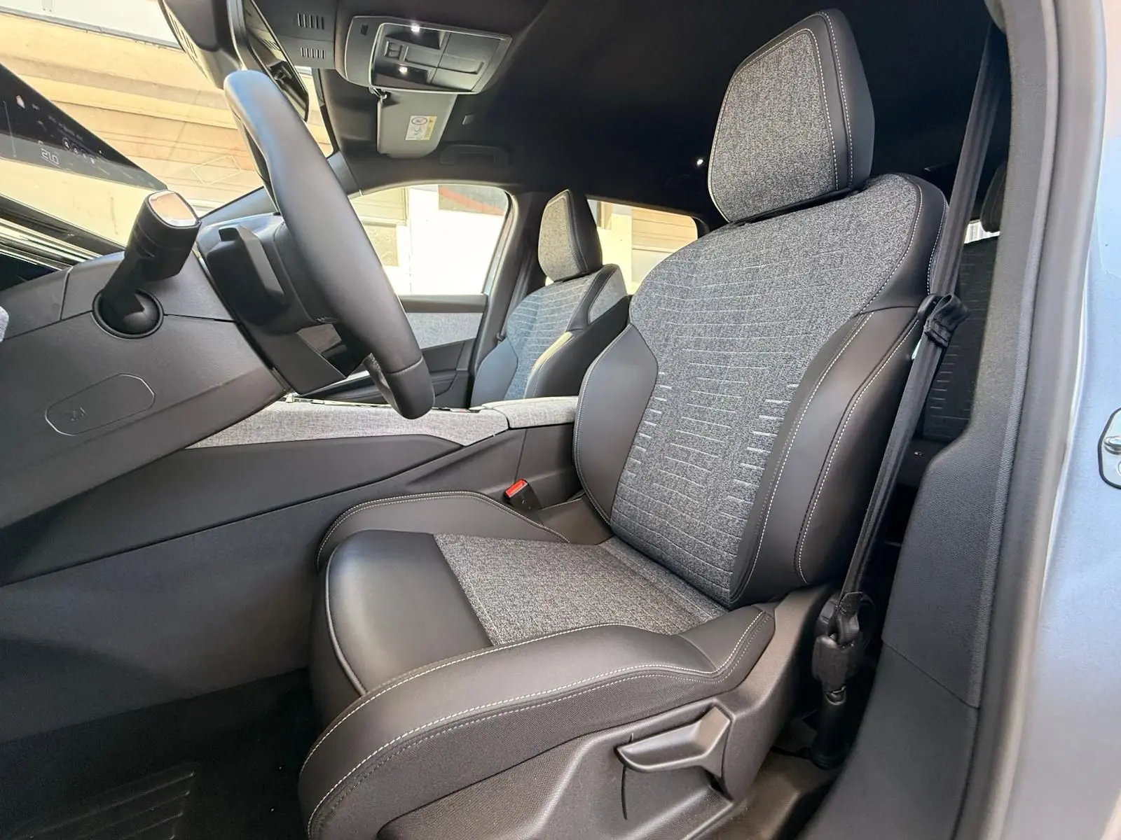 Vue intérieure côté conducteur du Peugeot 5008 1.2 Hybrid 145 Allure, sièges tissu gris et cuir noir.