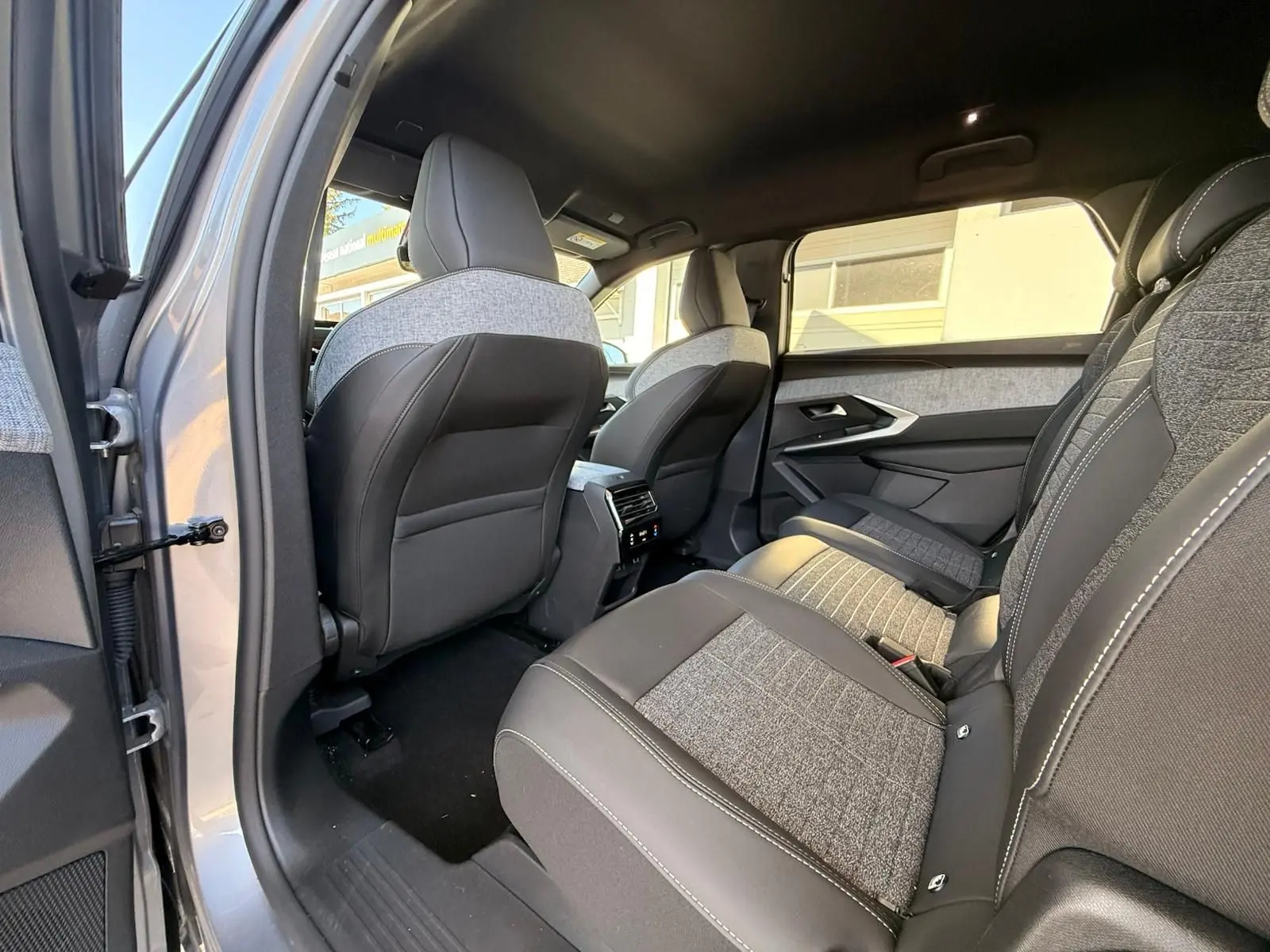 Vue intérieure arrière côté gauche du Peugeot 5008 gris Artense 2025, sièges tissu et cuir avec surpiqûres blanches.