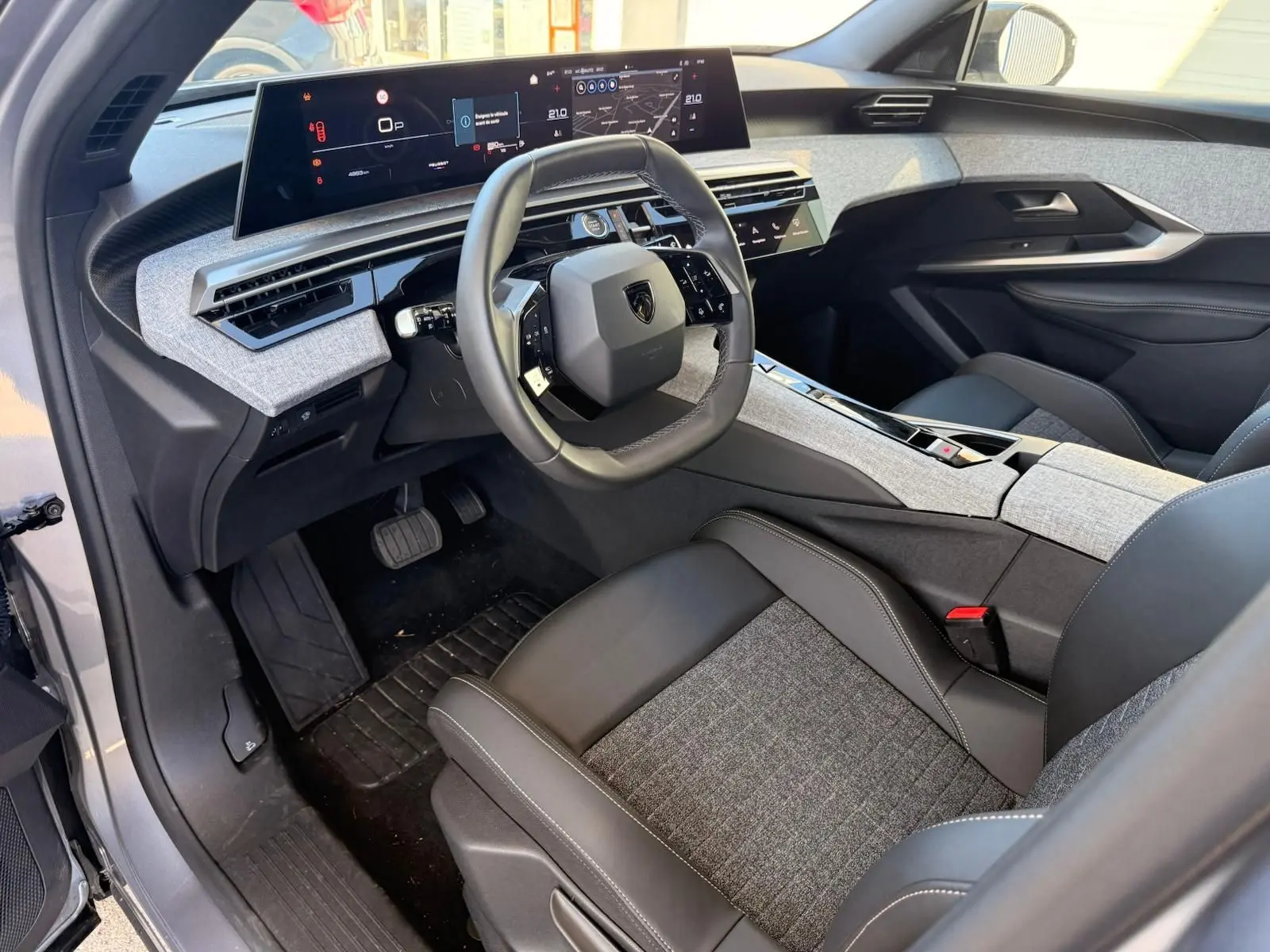 Vue intérieure côté conducteur du Peugeot 5008 1.2 Hybrid 145 Allure 2025, avec tableau de bord numérique et sellerie gris clair et noir.