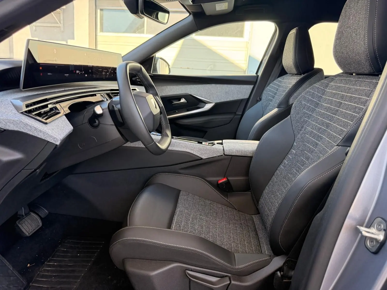 Vue intérieure côté conducteur du Peugeot 5008 1.2 Hybrid 145 Allure 2025, sièges tissu gris et cuir noir, tableau de bord moderne.