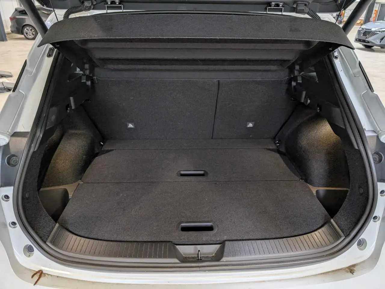 Coffre ouvert du Nissan Qashqai blanc nacré 2025, montrant un espace de chargement plat et bien fini.