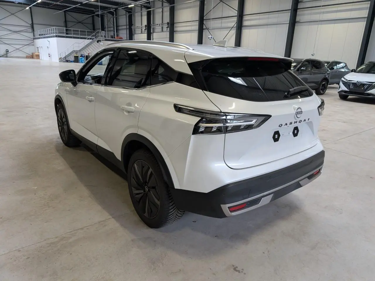 Vue 3/4 arrière droite du Nissan Qashqai blanc nacré 2025 avec toit panoramique et jantes alliage noires.