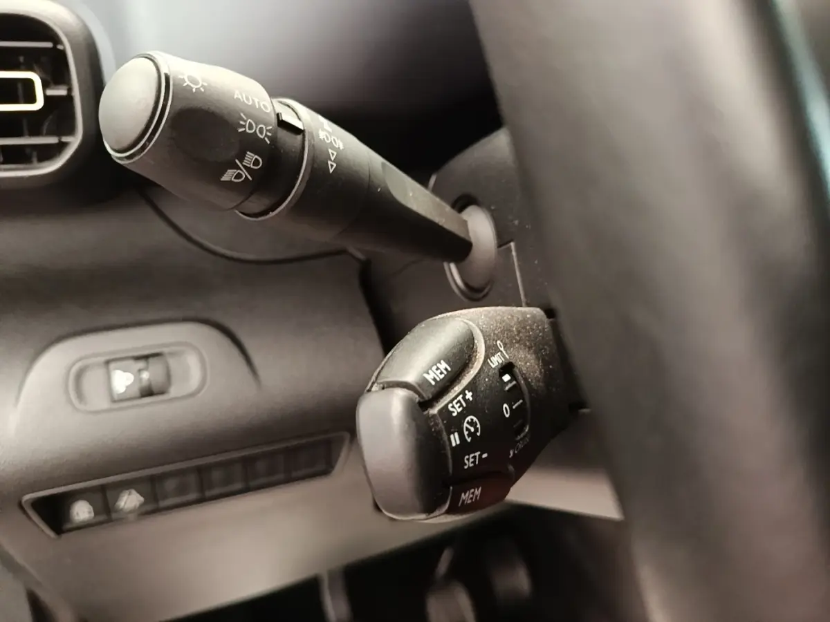 Gros plan sur les commandes au volant cuir du Peugeot Rifter blanc, avec réglages feux et régulateur de vitesse visibles.