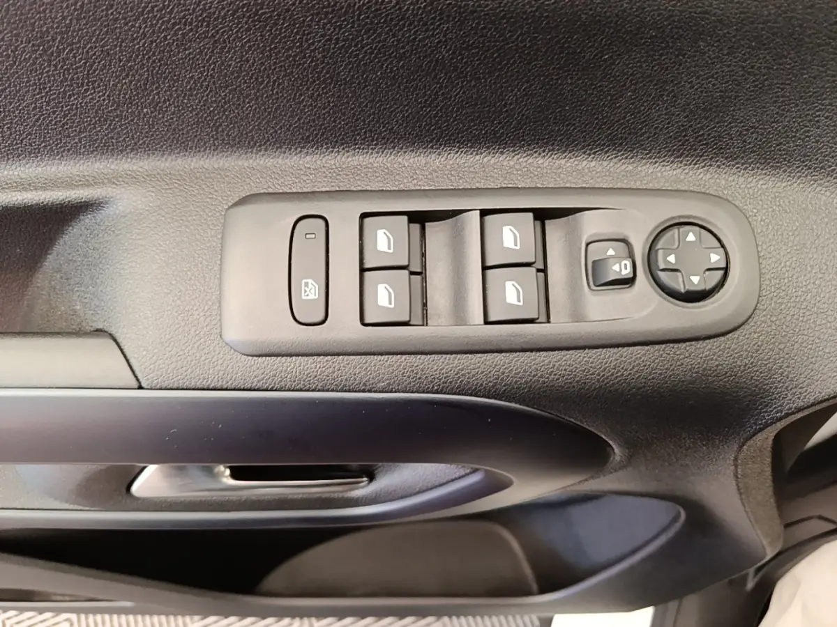 Gros plan sur la commande des vitres électriques et des rétroviseurs sur la porte côté conducteur d’un Peugeot Rifter blanc.
