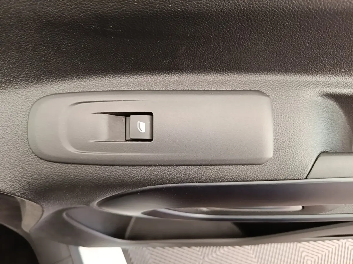 Gros plan sur le bouton de commande de la vitre électrique sur la porte intérieure noire d’un Peugeot Rifter blanc.