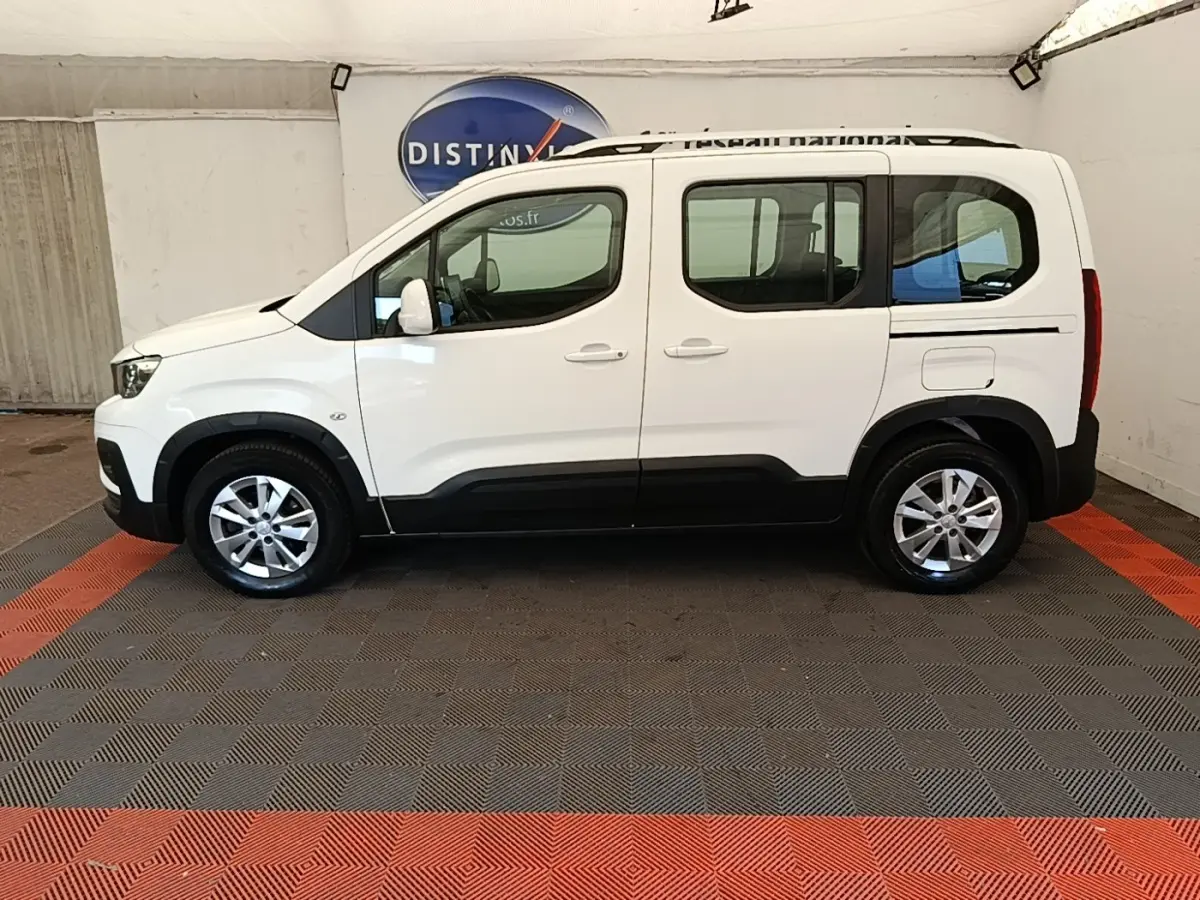 Vue latérale droite d'un Peugeot Rifter blanc 2020 avec barres de toit chromées et jantes alliage.
