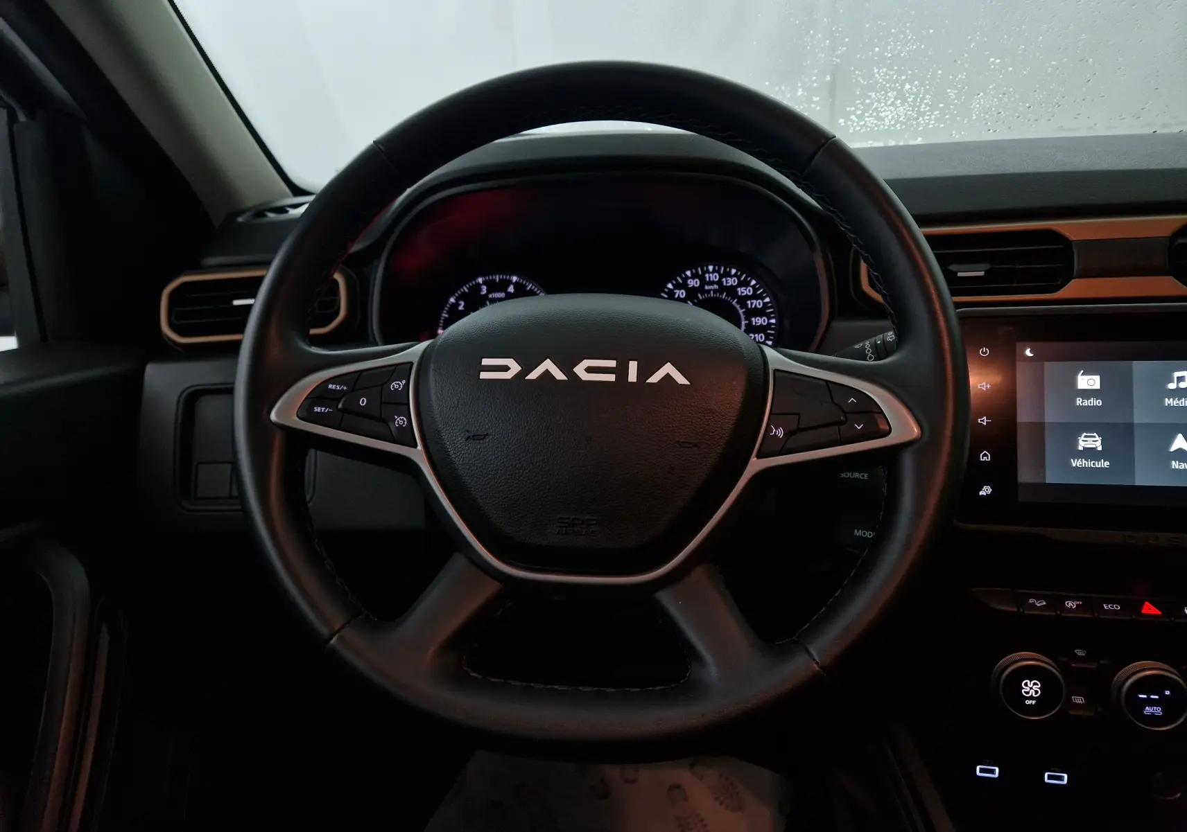 Vue rapprochée du volant noir du Dacia Duster 2024 avec commandes intégrées et tableau de bord lumineux.