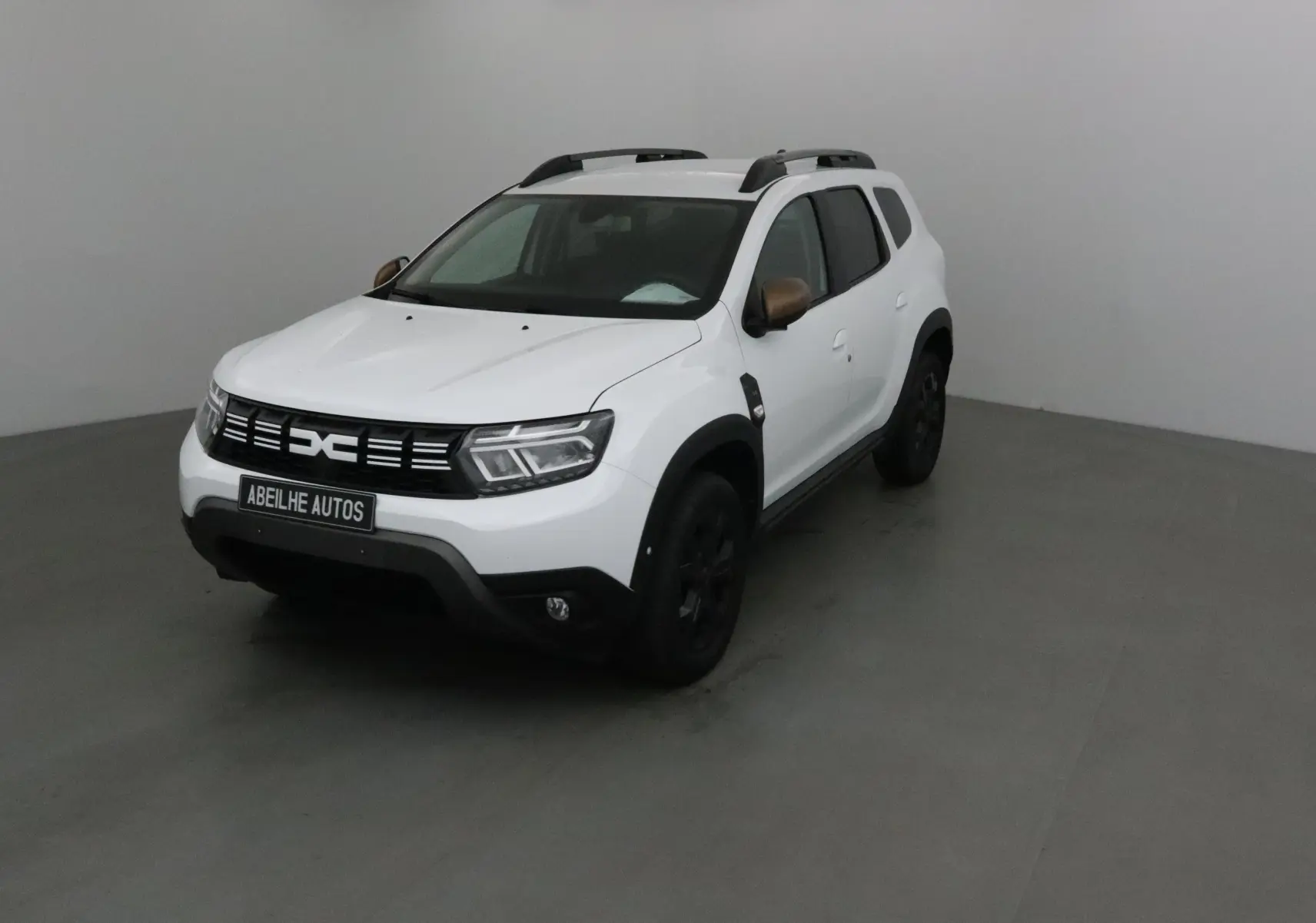 Vue 3/4 avant d'un Dacia Duster blanc 2024 avec rétroviseurs bronze et jantes noires en intérieur neutre.