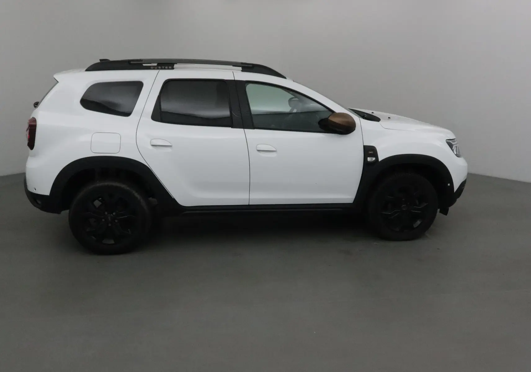 Profil côté droit d'un Dacia Duster 4x4 blanc 2024 avec jantes noires et coques de rétroviseurs marron.