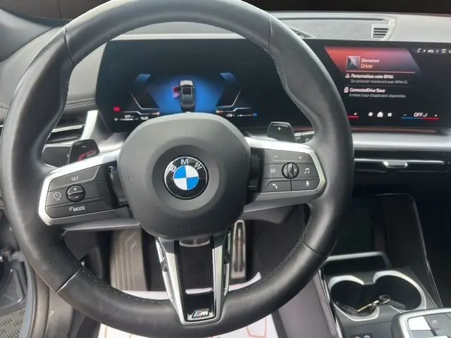 Vue rapprochée du volant M-Sport en cuir noir du BMW X1 2024 avec tableau de bord digital et écran central.