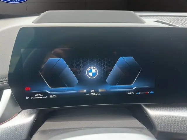 Affichage numérique du tableau de bord BMW X1 2024 en vue frontale, avec logo central et informations de conduite visibles.