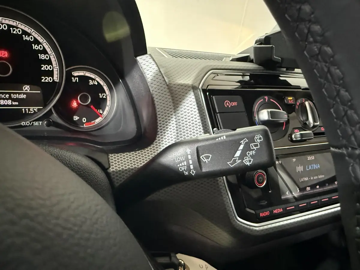 Vue rapprochée du tableau de bord et du commodo d'essuie-glace d'une Volkswagen Up gris foncé, avec affichage digital et commandes climatisation.