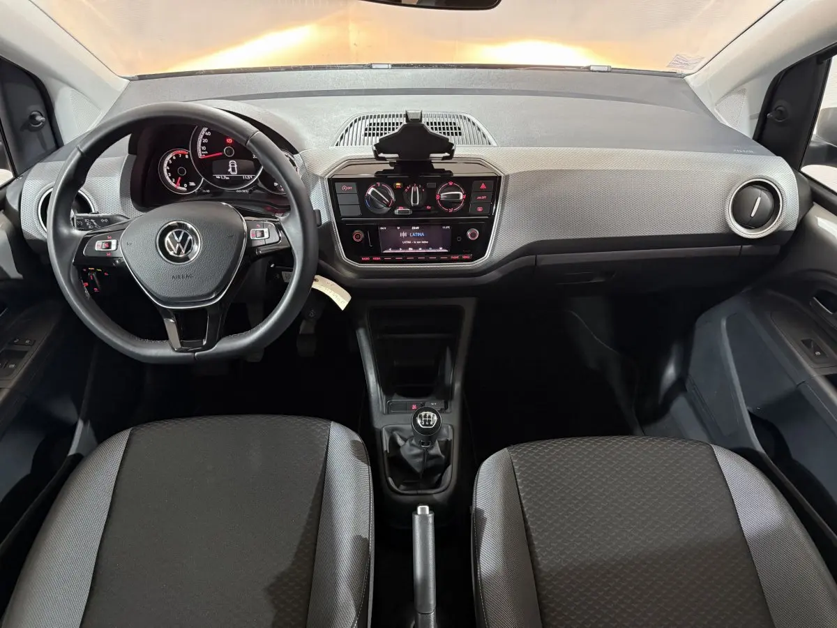 Vue intérieure avant du Volkswagen Up 1.0 65 Active avec tableau de bord clair, volant cuir et boîte manuelle.