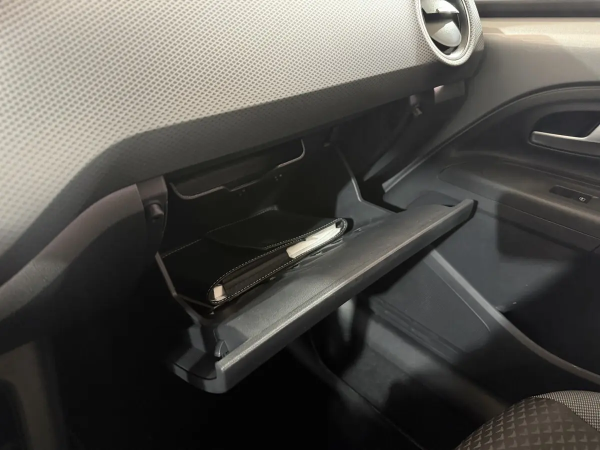 Gros plan sur la boîte à gants ouverte côté passager du Volkswagen Up gris foncé, avec un carnet à l'intérieur.