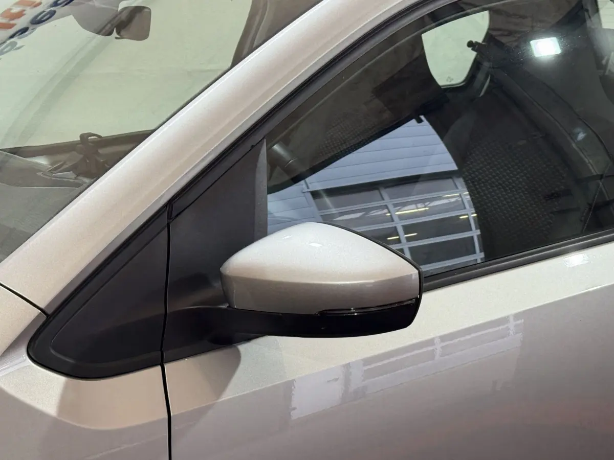 Gros plan sur le rétroviseur côté gauche d'une Volkswagen Up gris foncé avec reflet d'un bâtiment en arrière-plan.