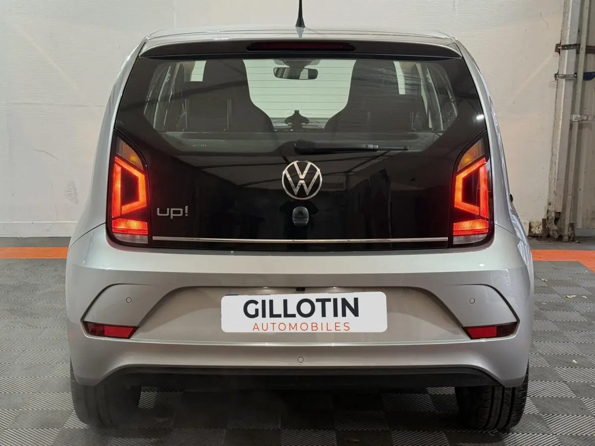 Vue arrière d'une Volkswagen Up! gris foncé avec feux arrière allumés et logo VW bien visible.
