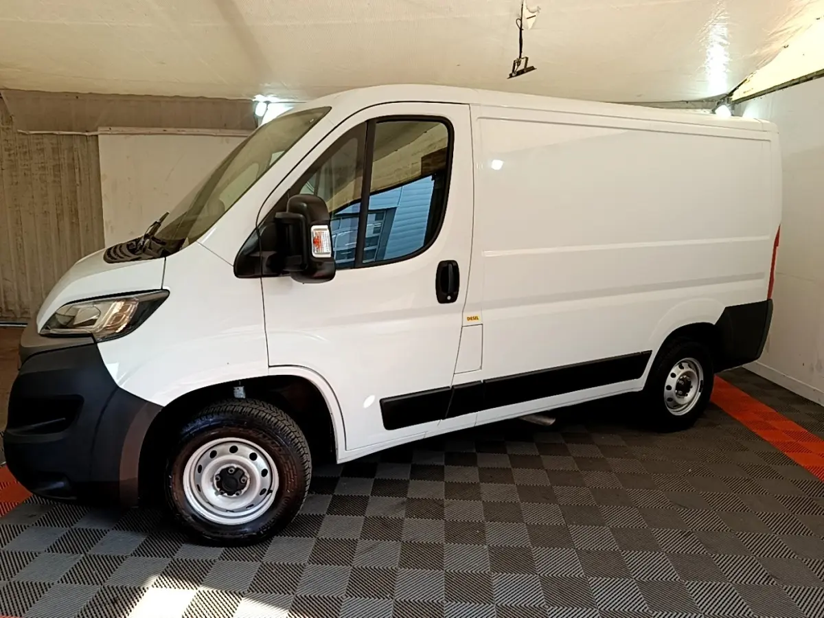 Vue latérale gauche d’un FIAT Ducato Fourgon blanc 2021 avec jantes acier et rétroviseurs noirs dans un garage.
