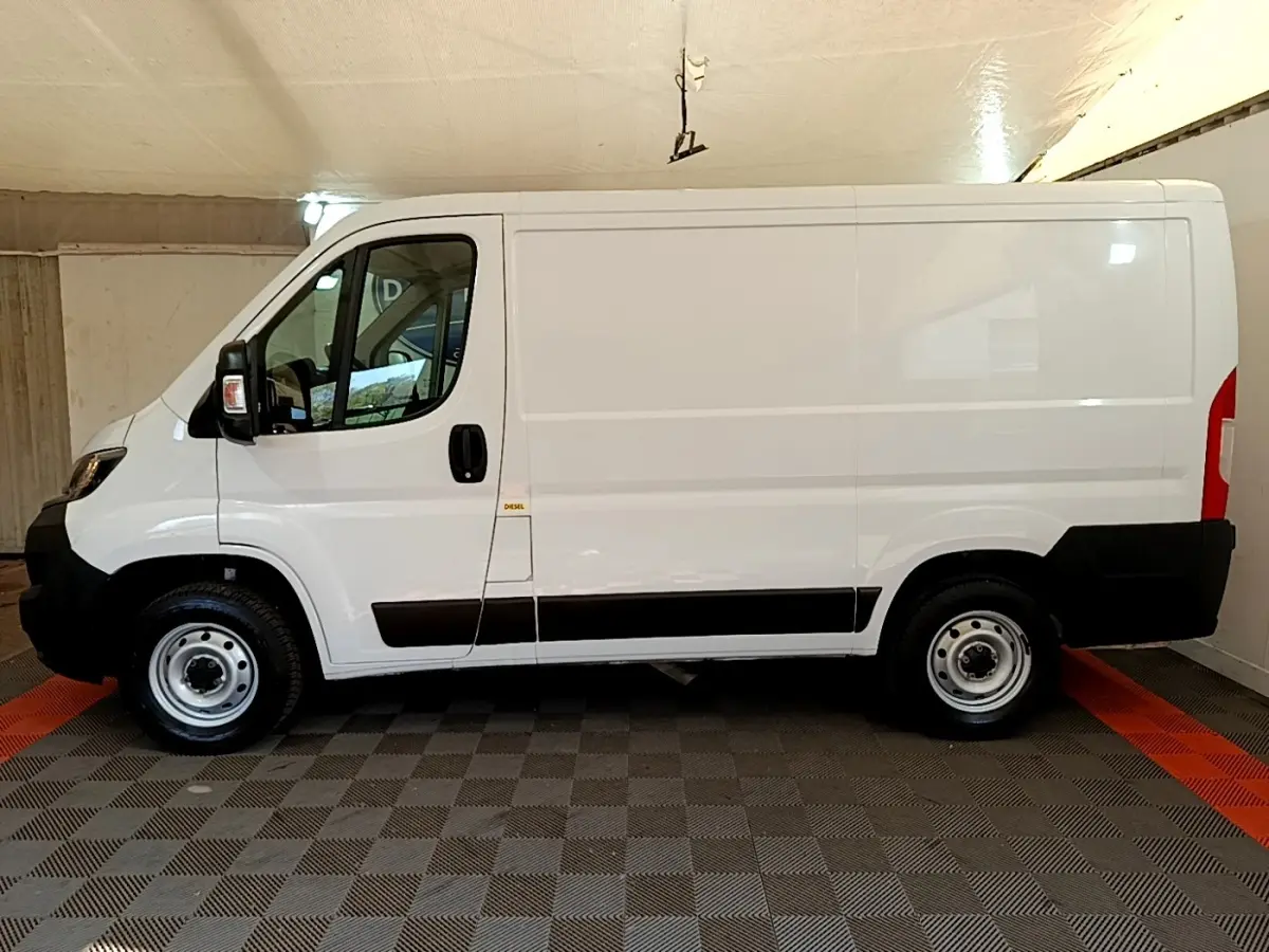 Vue latérale gauche d’un utilitaire blanc FIAT Ducato Fourgon 2021 avec protections noires et jantes acier simples.