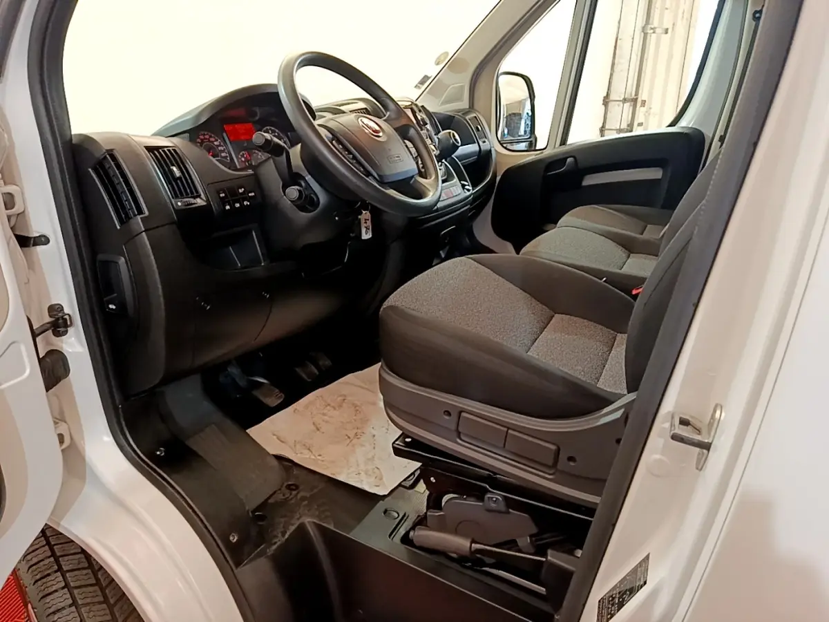 Vue intérieure côté conducteur du Fiat Ducato Fourgon blanc 2021, montrant le volant multifonctions et les sièges gris.