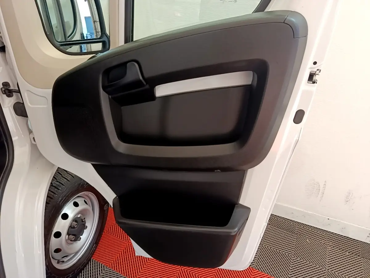 Vue rapprochée de la porte avant gauche ouverte d’un FIAT Ducato Fourgon blanc, avec rangement intégré noir.