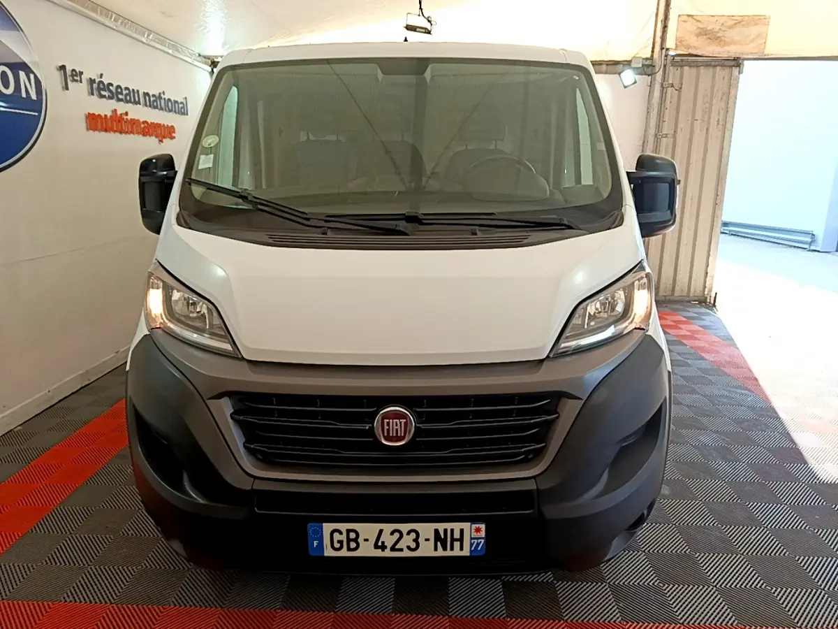 Vue frontale d’un FIAT Ducato Fourgon blanc avec calandre noire et phares allumés dans un garage.