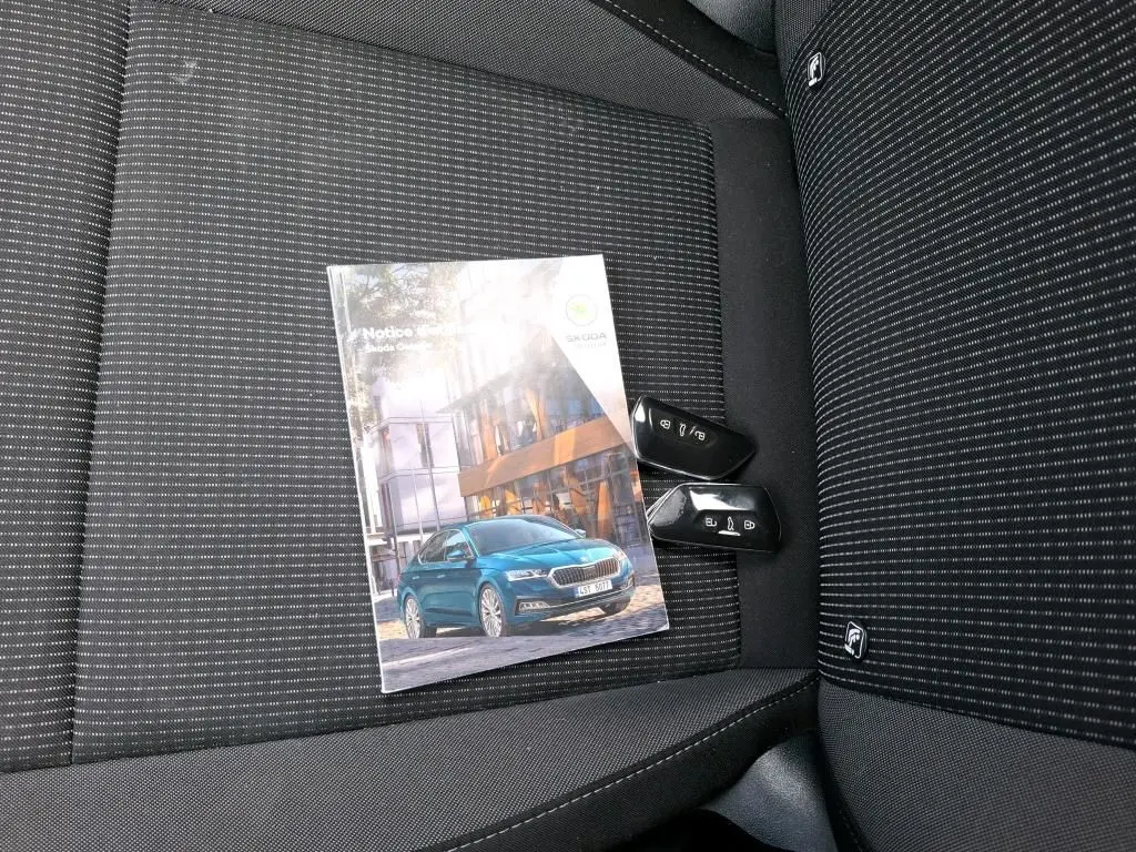 Notice d'utilisation SKODA Octavia posée sur un siège tissu noir à rayures fines avec deux clés de voiture noires.