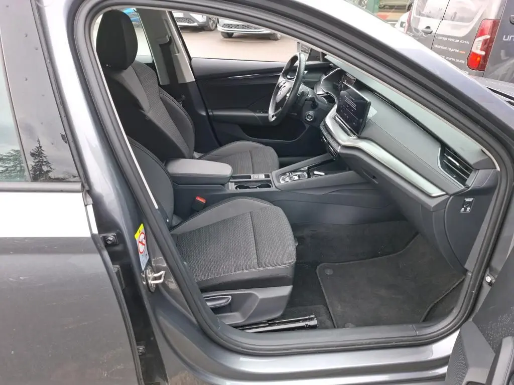 Vue intérieure côté conducteur de la Skoda Octavia Combi gris 2023, montrant sièges tissu et tableau de bord moderne.