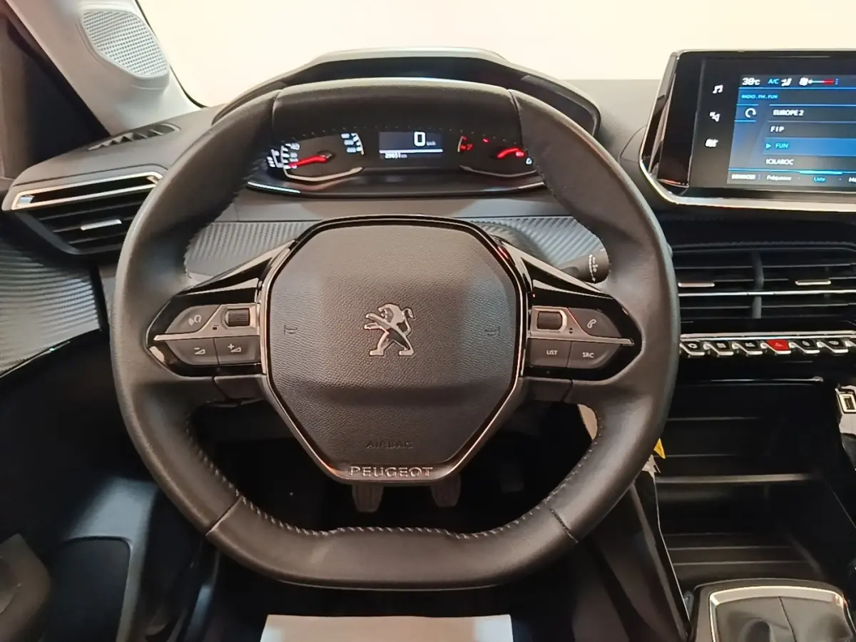 Vue intérieure centrée sur le volant cuir multifonctions de la Peugeot 208 2023 avec tableau de bord numérique et écran tactile.
