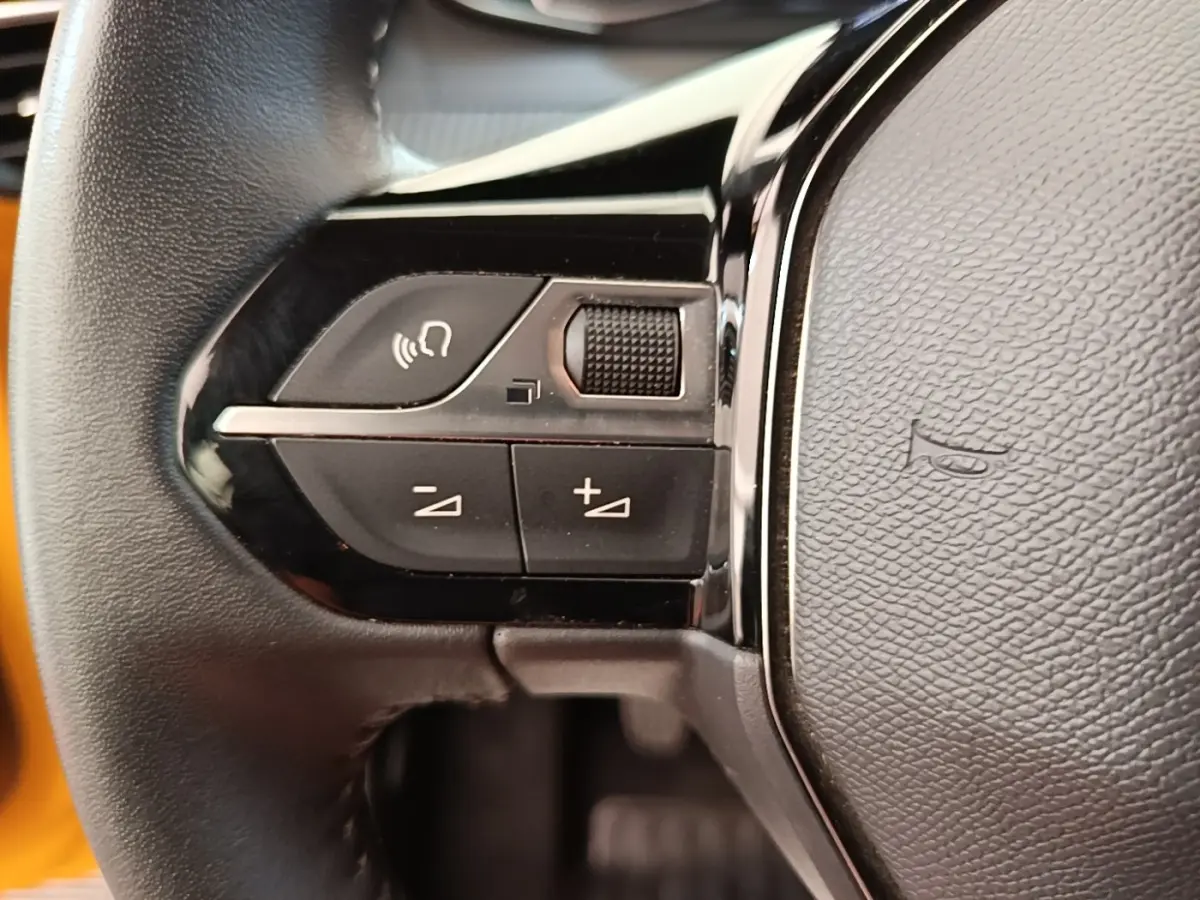 Gros plan sur le volant cuir noir multifonctions de la Peugeot 208 jaune, avec commandes audio intégrées.