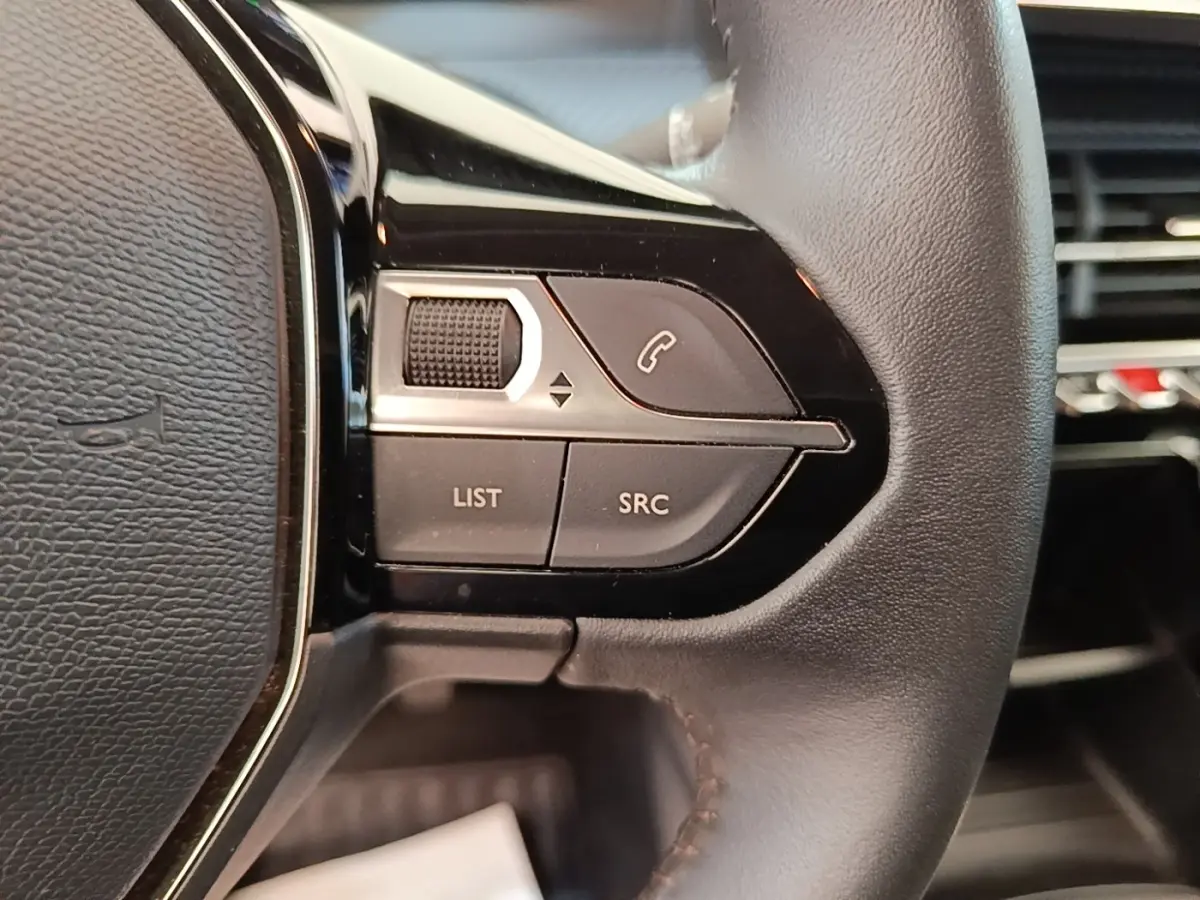 Gros plan sur les commandes gauche du volant cuir noir de la Peugeot 208 jaune, avec boutons multifonctions et molette.